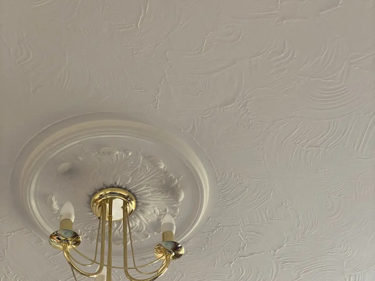 Chandelier hanging from a textured white ceiling with a plaster surround