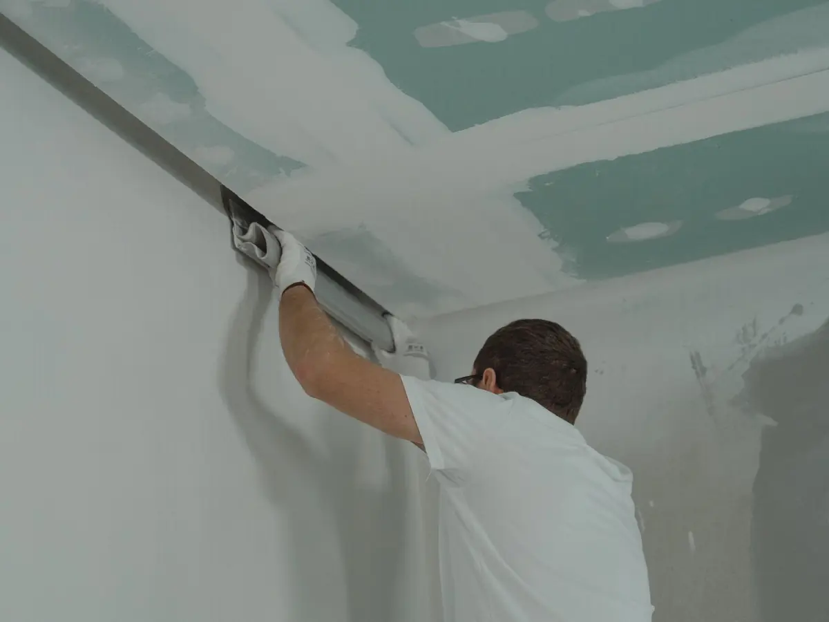 Plasterer fixing a sheet of plasterboard to a wall inside a house