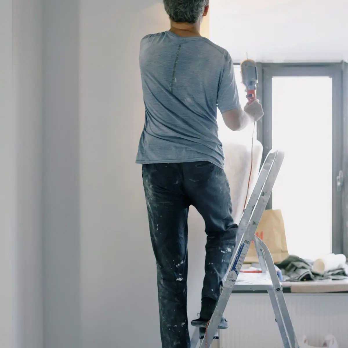 Working from a step ladder to finish a wall beside a window