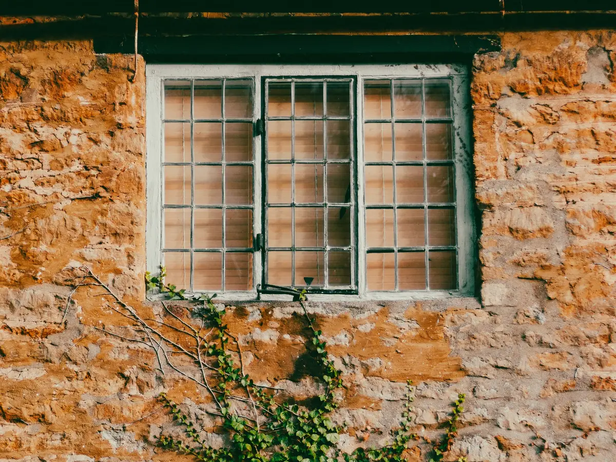 Old rubble stone wall with a small timber window and ivy