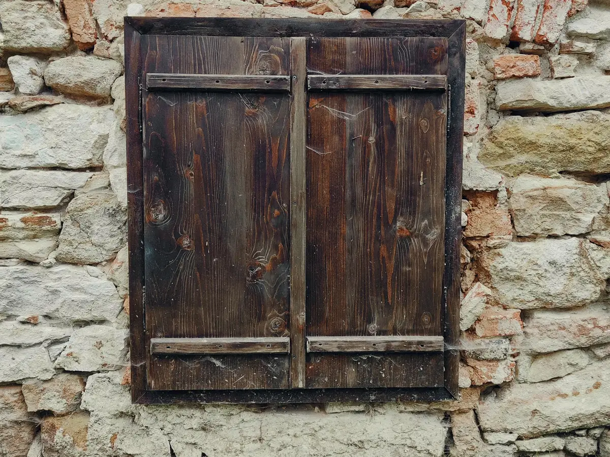 Old lime-plastered stone wall with weathered timber shutters