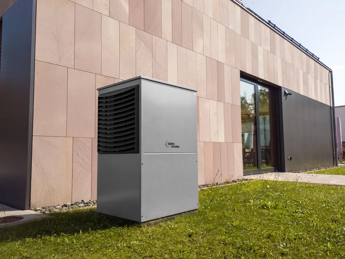 Air source heat pump unit beside a modern house wall