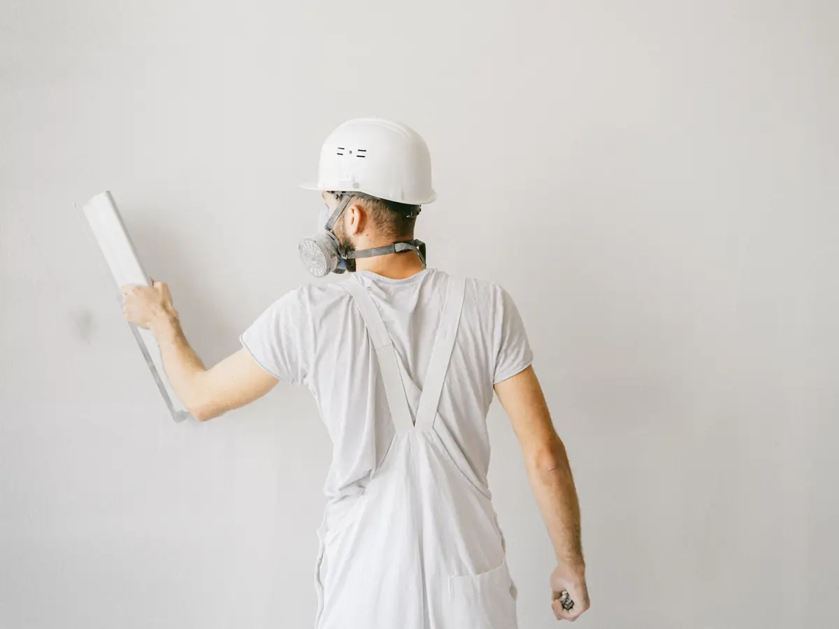 Plasterer in safety gear working a trowel across a white wall