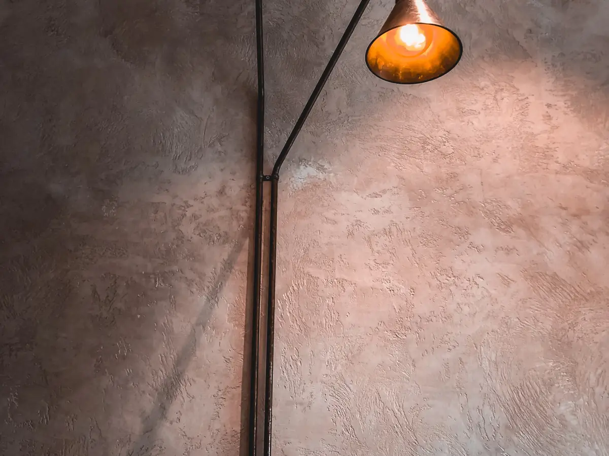 Industrial wall lamp casting warm light across a mottled plaster wall